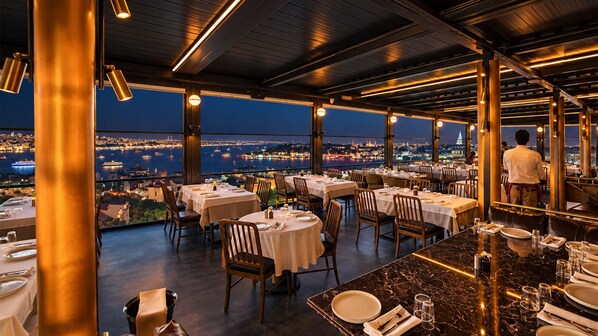 A restaurant with tables set for dining, overlooking a cityscape at night. - Ring Stone Hotels Bosphorus (Istanbul)