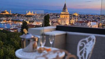 Un balcón con mesa y sillas que da a una vista panorámica de la ciudad, con edificios históricos y el mar.