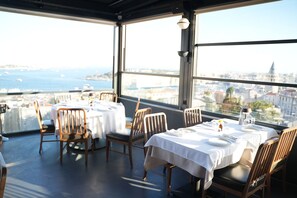 A restaurant with tables set for dining, large windows offering a view of the city and sea, and a modern interior design. - Ring Stone Hotels Bosphorus (Istanbul)