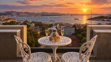 A balcony with a table set for two, overlooking a cityscape at sunset.