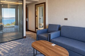 A hotel room with a sofa, a small wooden table, and a glass door leading to a balcony with a view. - Ring Stone Hotels Bosphorus (Istanbul)