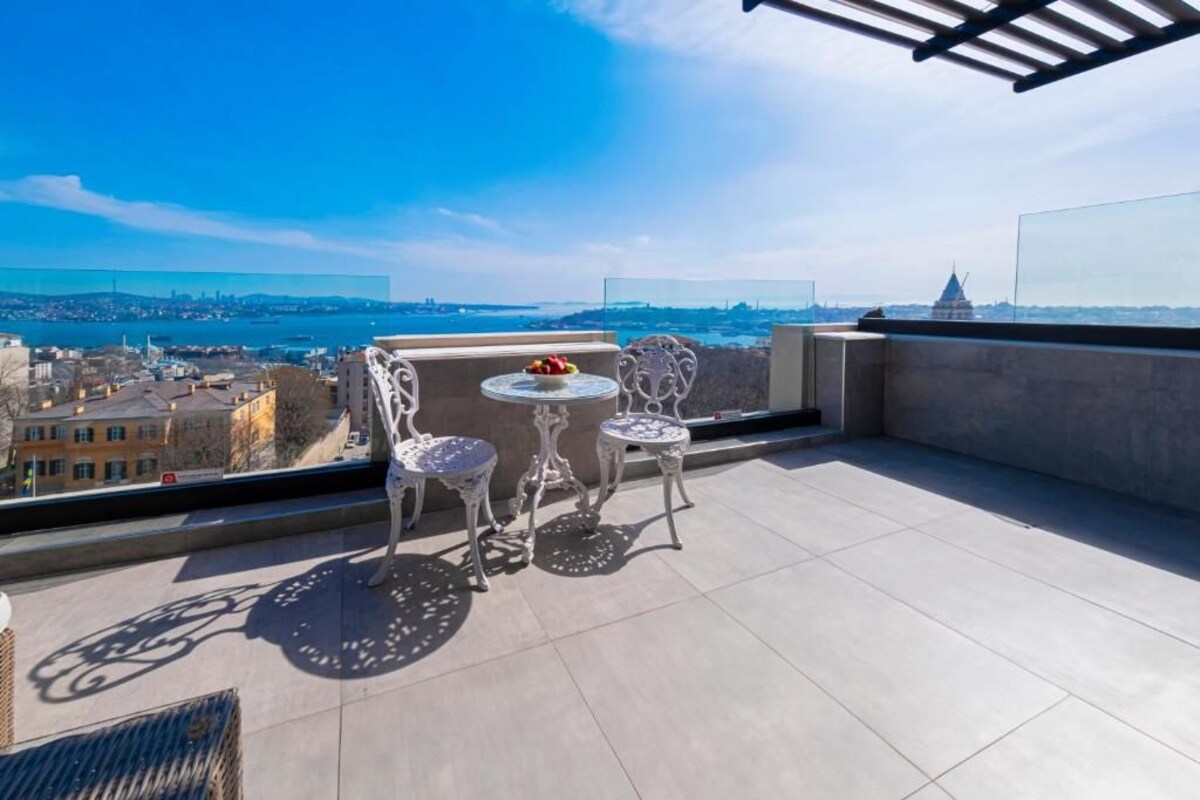 A balcony with a table and chairs, overlooking a cityscape and a body of water.