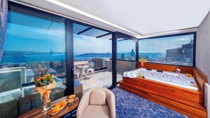 Une chambre d’hôtel moderne dotée d’une grande fenêtre donnant sur la ville, d’une baignoire en bois, d’un coin salon avec une table et des chaises, et d’un vase décoratif rempli de fleurs.