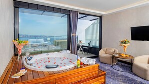 Une chambre d’hôtel moderne dotée d’une grande baignoire, offrant une vue sur la ville, d’un téléviseur à écran plat et d’un coin salon confortable.