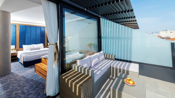 Une chambre d’hôtel moderne dotée d’un balcon, d’un lit, d’un coin salon et d’une table pour le petit-déjeuner avec des fruits.