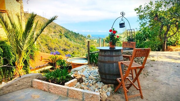 A rustic outdoor seating area with a wooden chair, a round table, and a barrel. - Country house with pool sea view (camporosso)