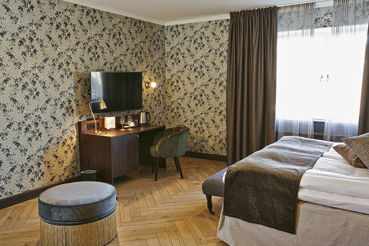 Une chambre d’hôtel comprenant un lit, un bureau avec une chaise, une télévision et une fenêtre avec des rideaux.