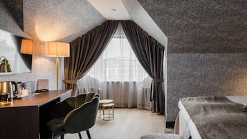 Ein modernes Hotelzimmer mit Schreibtisch, zwei Stühlen, einem Bett und einem großen Fenster mit Vorhängen.