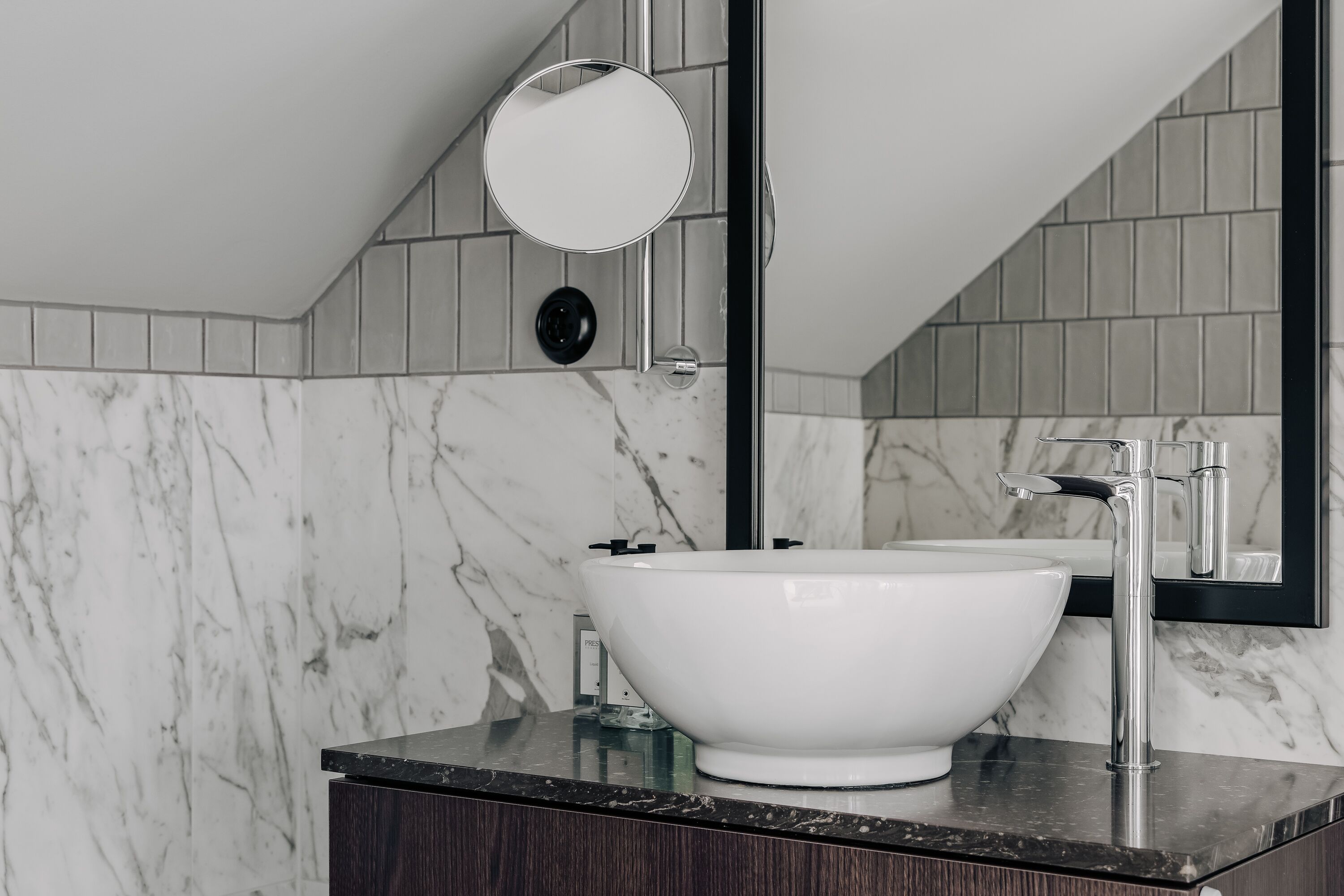 A bathroom with a white marble sink, a round mirror, and a black-framed mirror.