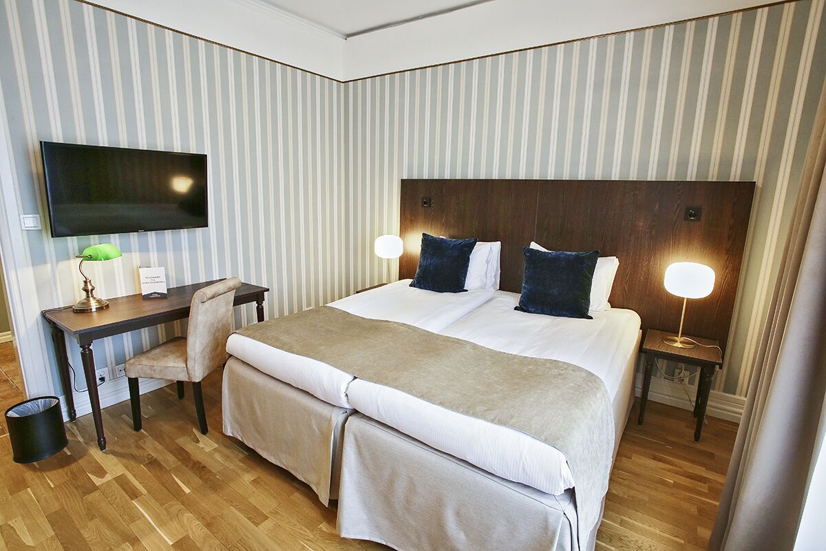 A hotel room with a large bed, a desk with a chair, a television, and two bedside lamps.