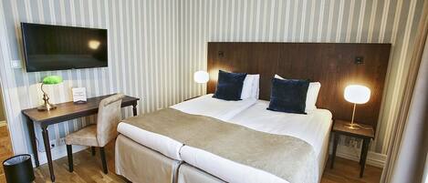 A hotel room with a large bed, a desk with a chair, a television, and two bedside lamps.
