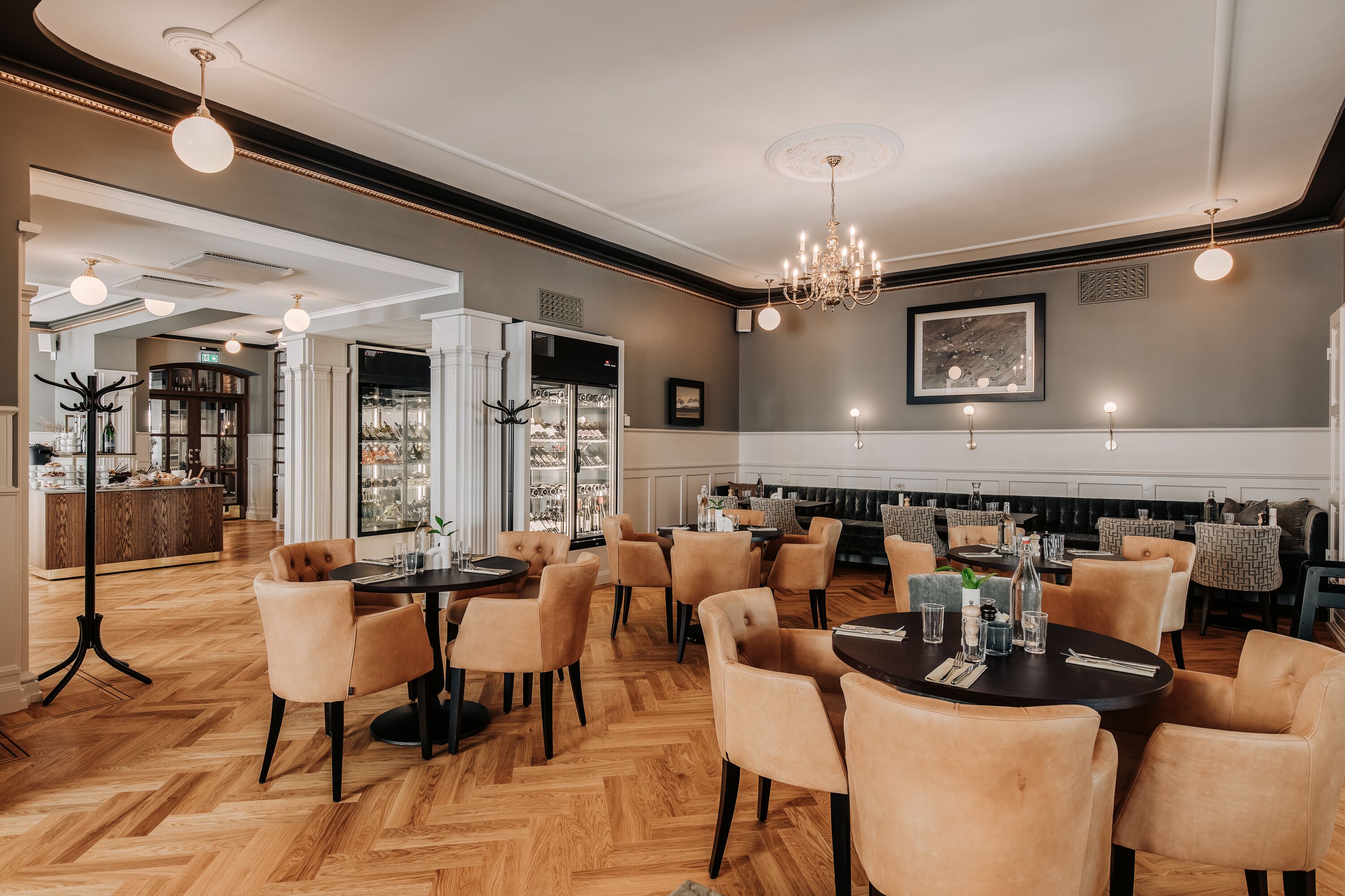 A restaurant with round tables and chairs, a chandelier, and a bar area.