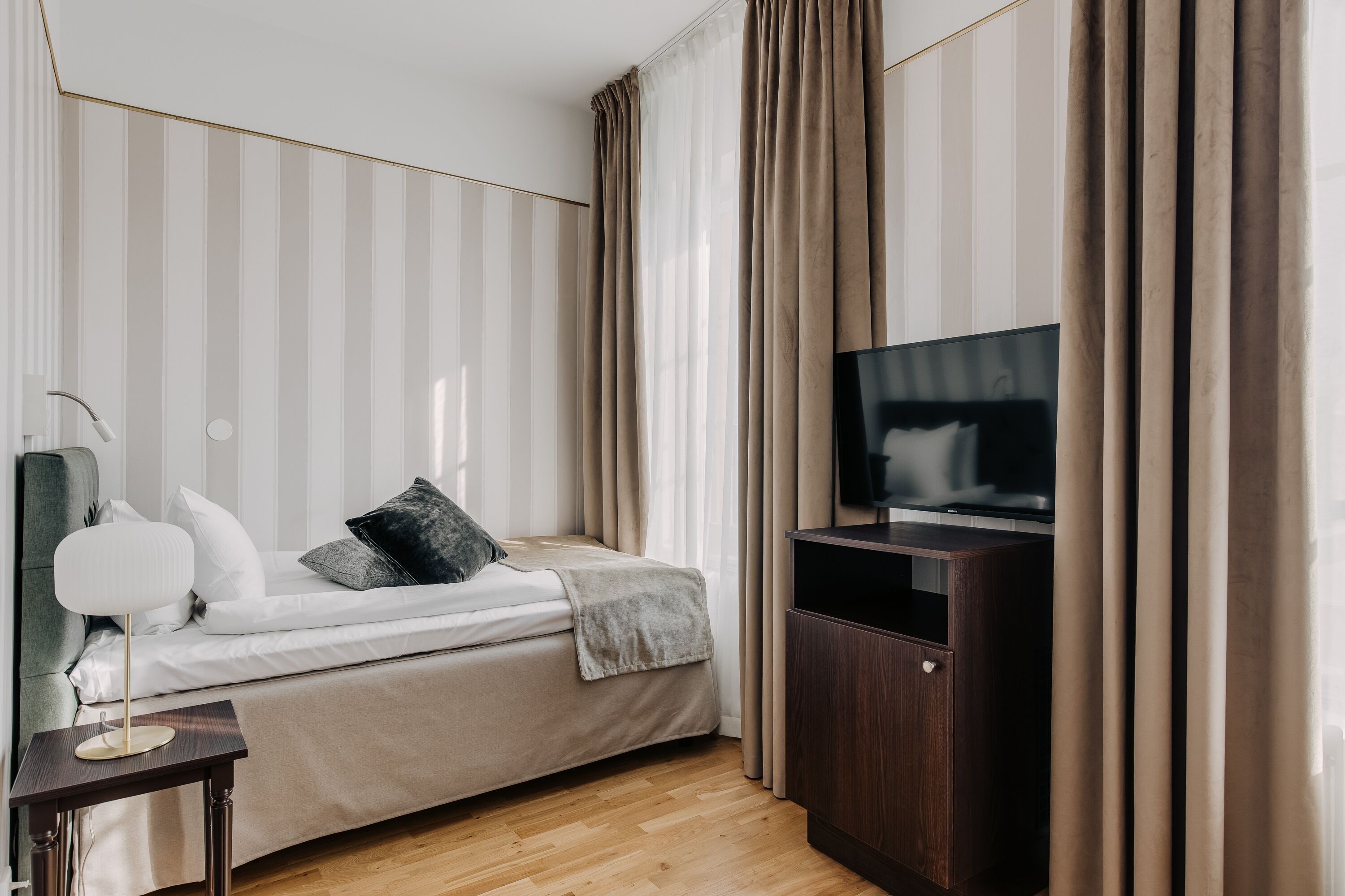 A modern hotel room with a bed, a TV, a bedside table, and a wardrobe.