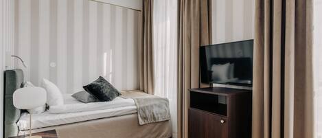 A modern hotel room with a bed, a TV, a bedside table, and a wardrobe.