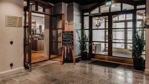 Un vestíbulo de hotel con una puerta de madera, una pizarra con texto y una planta en maceta.
