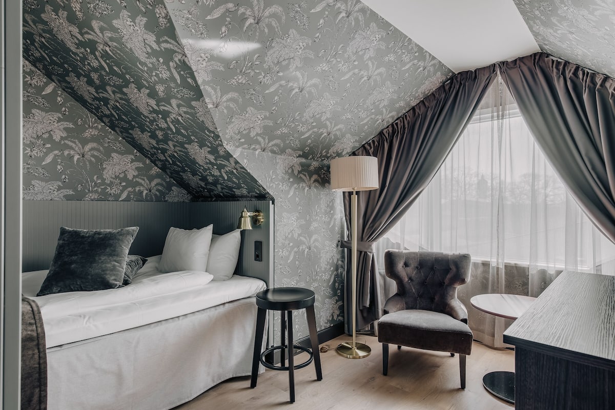 Quarto moderno com uma cama grande, um banquinho, uma cadeira e uma mesa.