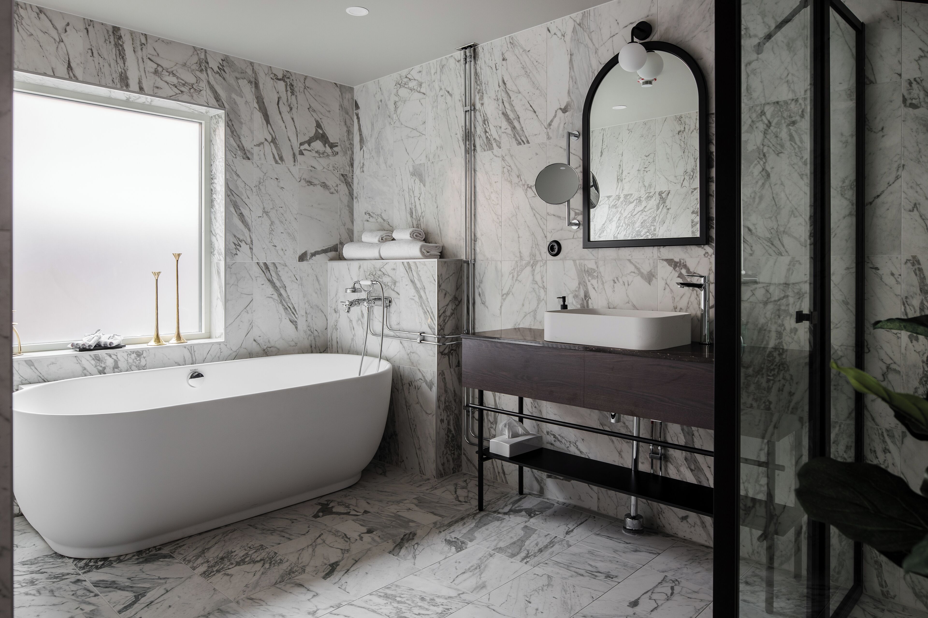 A modern bathroom with a freestanding bathtub, a vanity with a mirror, and marble walls.