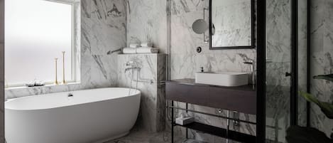 A modern bathroom with a freestanding bathtub, a vanity with a mirror, and marble walls.