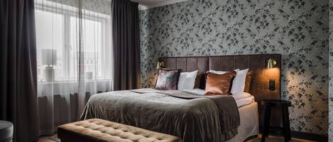 A bedroom with a large bed, a bench, a nightstand, and a window with curtains.