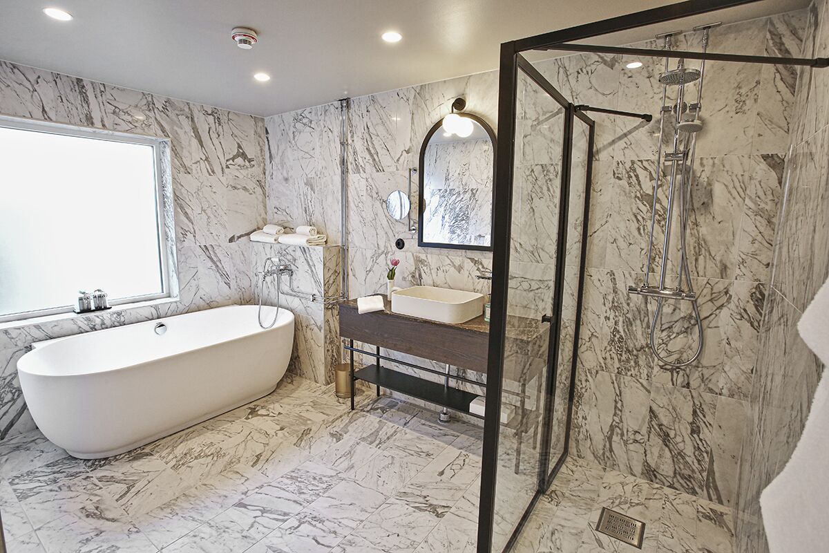 A modern bathroom with a freestanding bathtub, a glass-enclosed shower, and a marble-tiled floor.