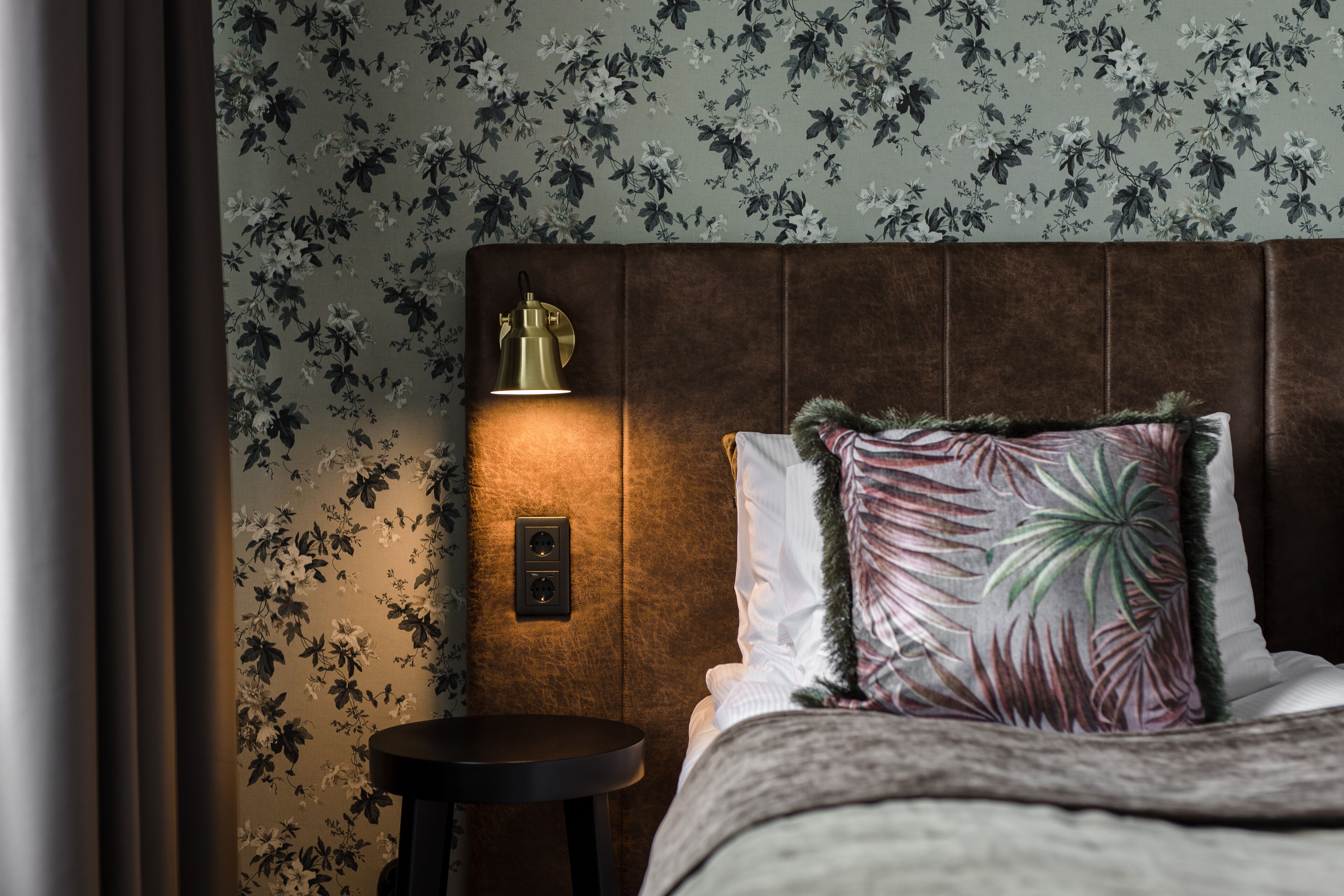 A neatly made bed with a floral-patterned pillow and a round bedside table.