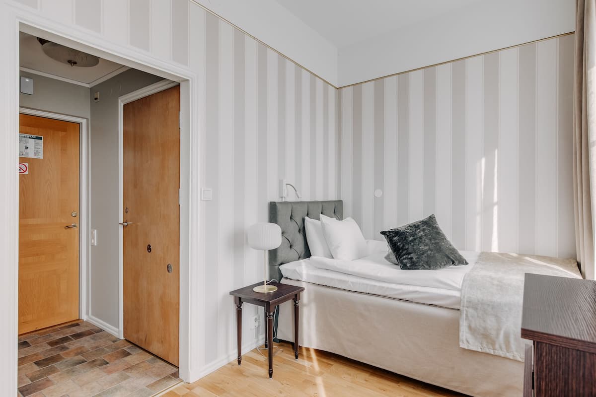 Um quarto com cama, mesa de cabeceira e uma porta.