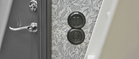 Uma porta com puxador prateado e olho de fechadura, e uma parede com papel de parede estampado com flores.