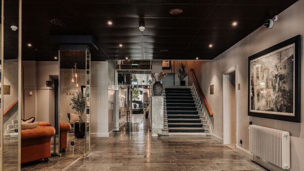 Un interior moderno con una escalera, una obra de arte enmarcada y una zona de estar con sofá y planta en maceta.