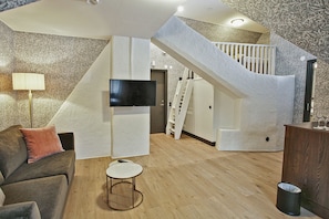 A modern living room with a flat-screen TV, a small round table, a sofa, and a staircase leading to an upper level. - Skara Stadshotell (Skara)