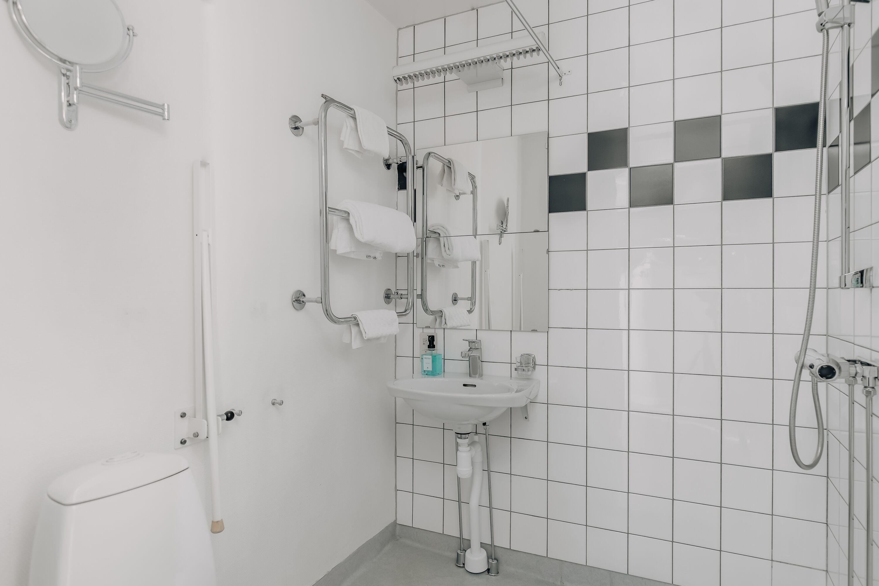Ett modernt badrum med ett vitt handfat, en spegel och en handdukshängare.