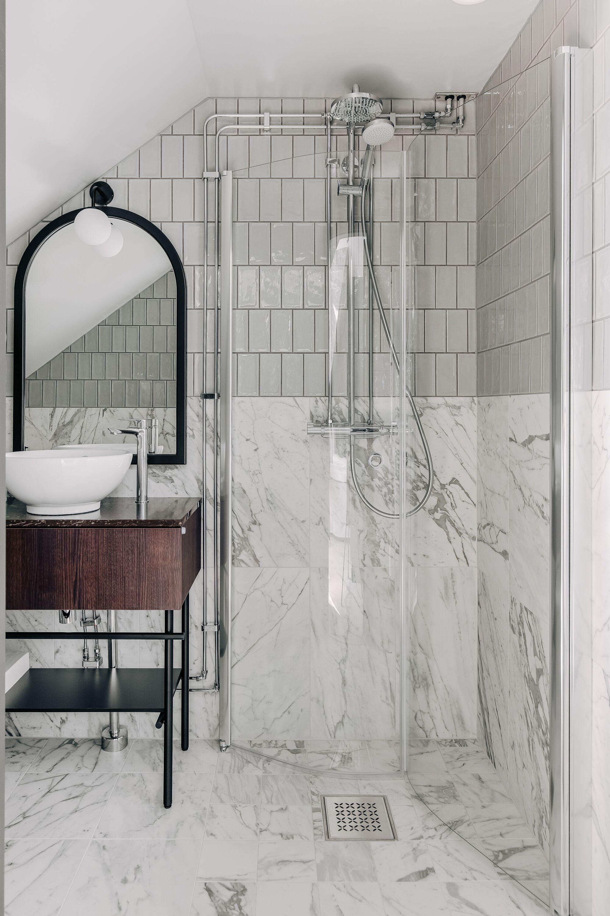 A modern bathroom with a glass-enclosed shower, a marble-tiled floor, and a dark wooden vanity with a white sink.