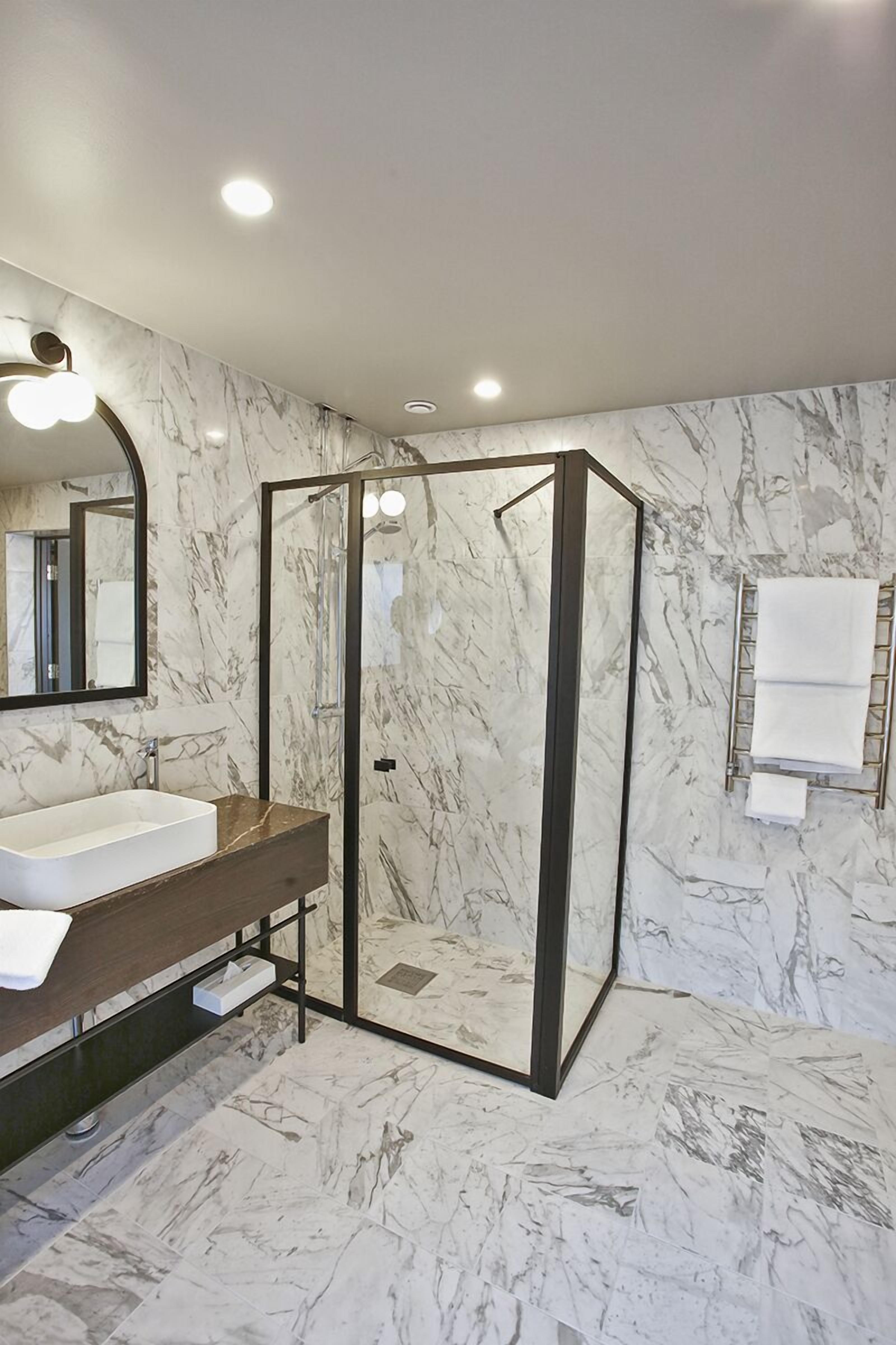 Un baño moderno con suelo de mármol, cabina de ducha con paredes de vidrio, lavamanos con mueble de madera y un perchero para toallas.