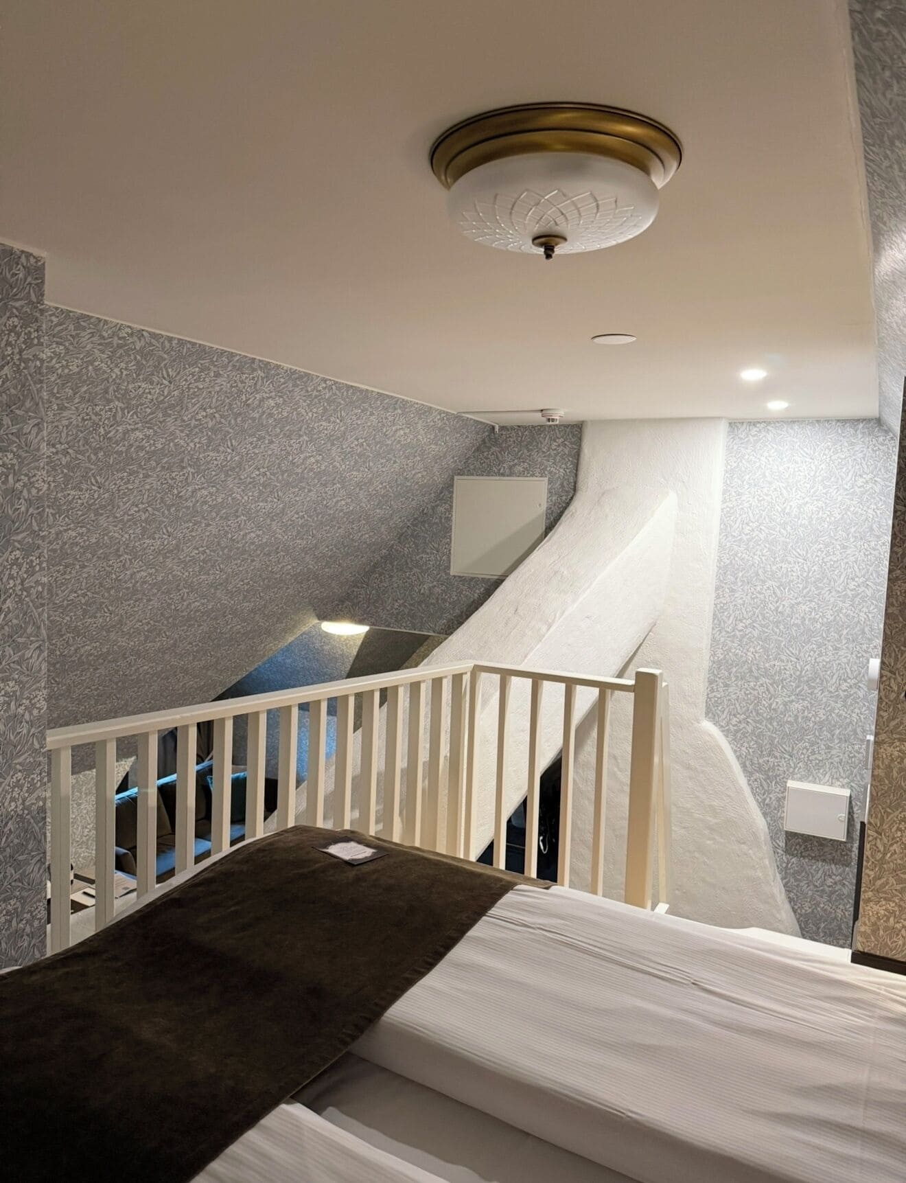 Une chambre à coucher avec un lit, une balustrade blanche, un luminaire au plafond et un mur à texture.