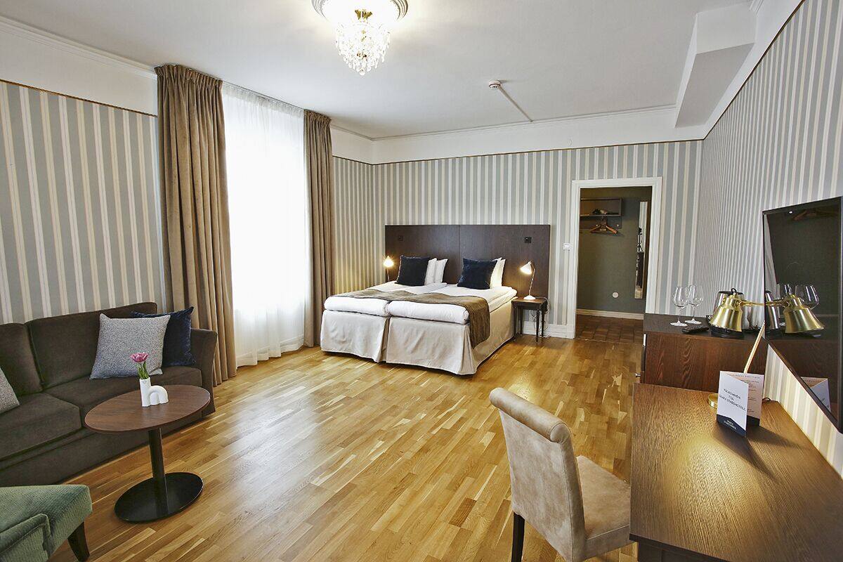 Quarto de hotel com uma cama grande, um sofá, uma pequena mesa redonda e uma escrivaninha com abajur.