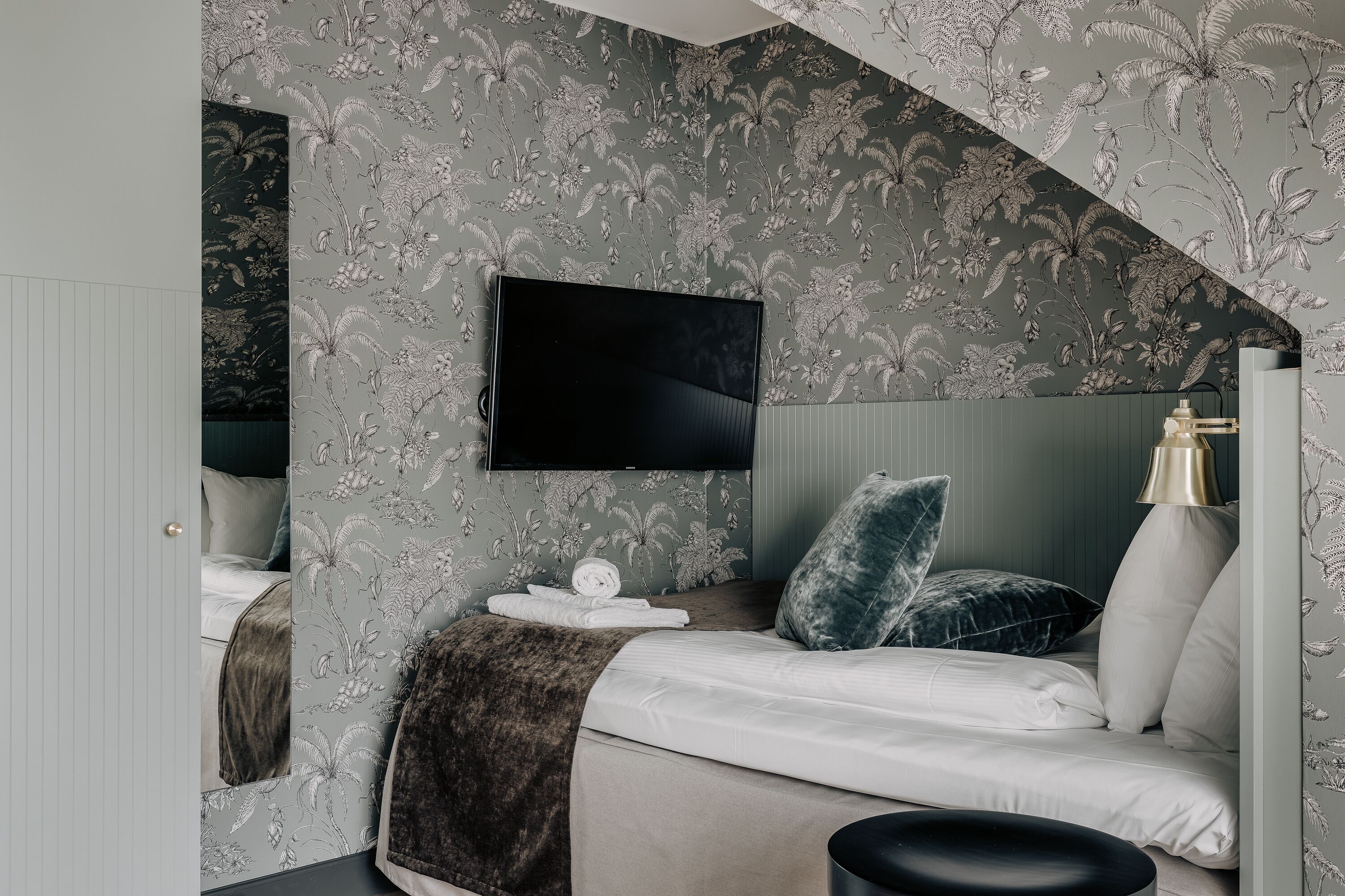 Ein Schlafzimmer mit Bett, einem flachbildfernseher an der Wand, einem Nachttisch mit Lampe und einem Fenster mit Vorhängen.