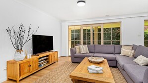 Uma sala de estar moderna com um amplo sofá seccional cinza, uma mesa de centro de madeira e uma TV sobre um suporte de madeira.