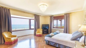 A hotel room with a large bed, two armchairs, a TV, and a view of the sea.
