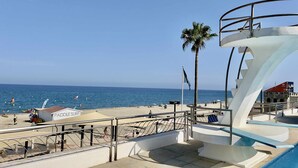 A beachside pool area with a sign for a paddle surf rental, a palm tree, and a clear view of the ocean.