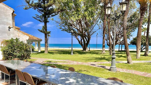 A long outdoor dining area with a view of the ocean, surrounded by trees and a gazebo.