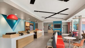 A modern hotel lobby with a reception desk, seating area, and a kitchen in the background. - avid hotel Fort Wayne North by IHG (Fort Wayne)