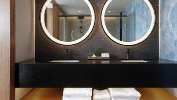 A bathroom with two sinks, a mirror, and a shelf with towels.