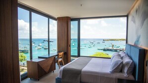 Une chambre d’hôtel moderne, dotée d’un grand lit, d’un bureau et offrant une vue sur la mer et les bateaux.