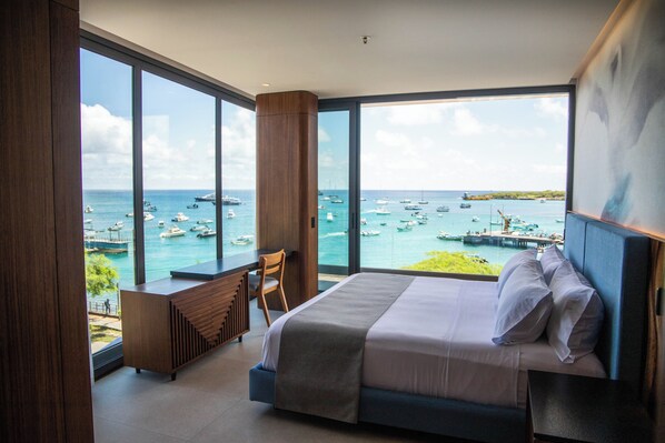 Une chambre d’hôtel moderne, dotée d’un grand lit, d’un bureau et offrant une vue sur la mer et les bateaux.