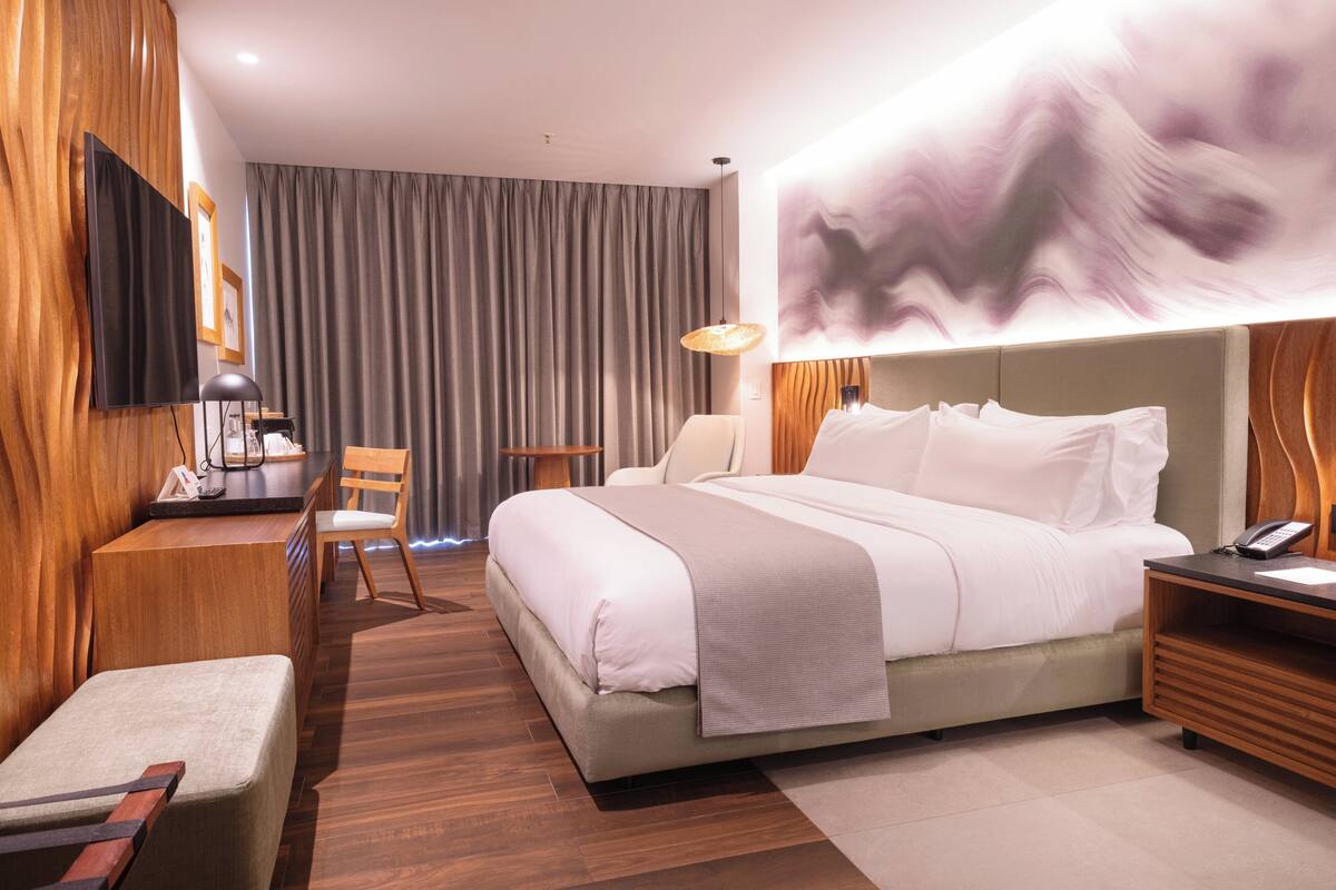 Une chambre d’hôtel avec un lit, un bureau et une chaise, un téléviseur et un grand tableau abstrait accroché au mur.