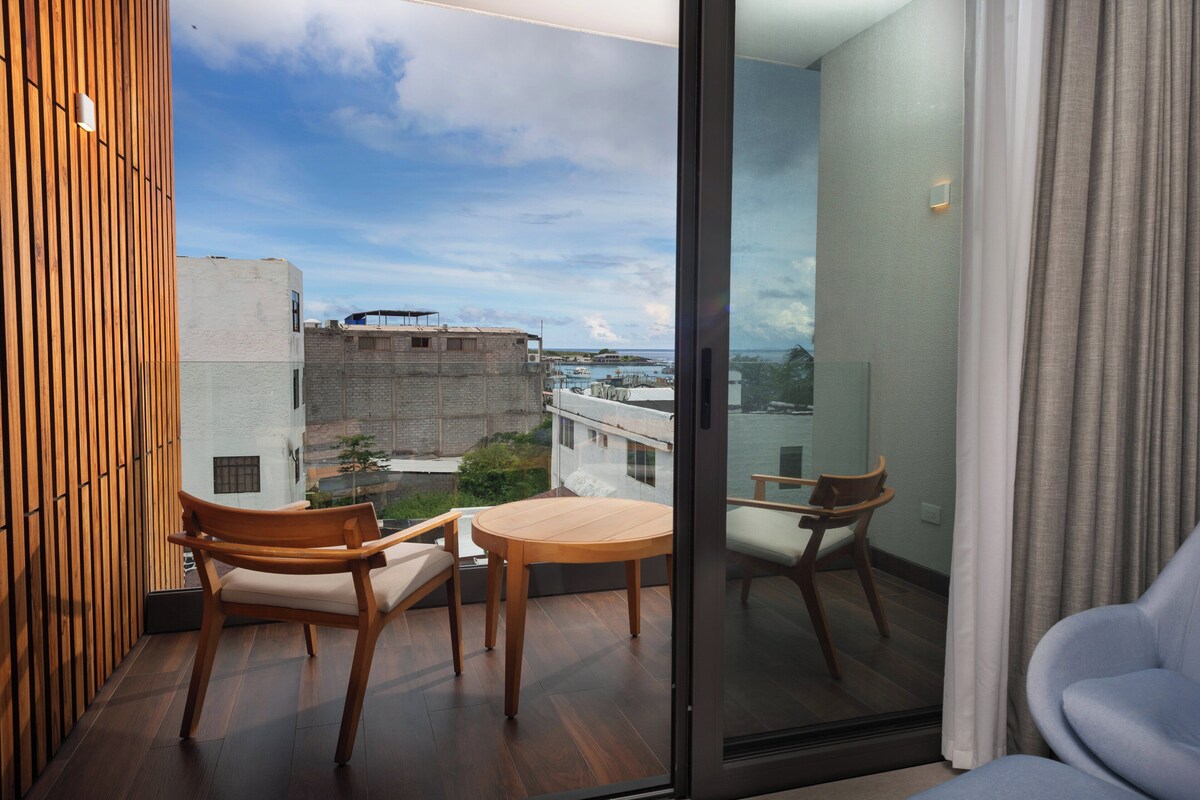 Ein Balkon mit Holzmöbeln, einer Glastür und Blick auf Gebäude und Wasser.
