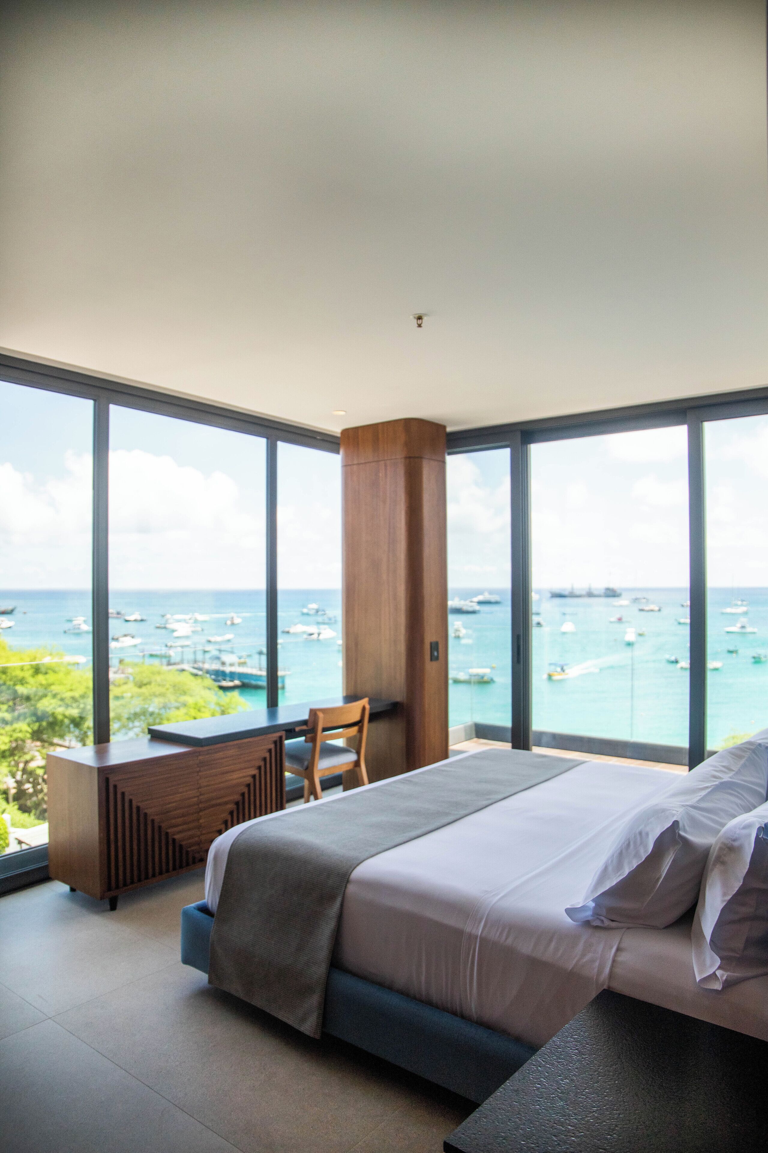 Un dormitorio moderno con una cama grande, un escritorio de madera y vista al mar.