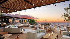 Un espace de restauration en plein air avec des tables et des chaises, un plafond en bois et une vue sur la mer au coucher du soleil.