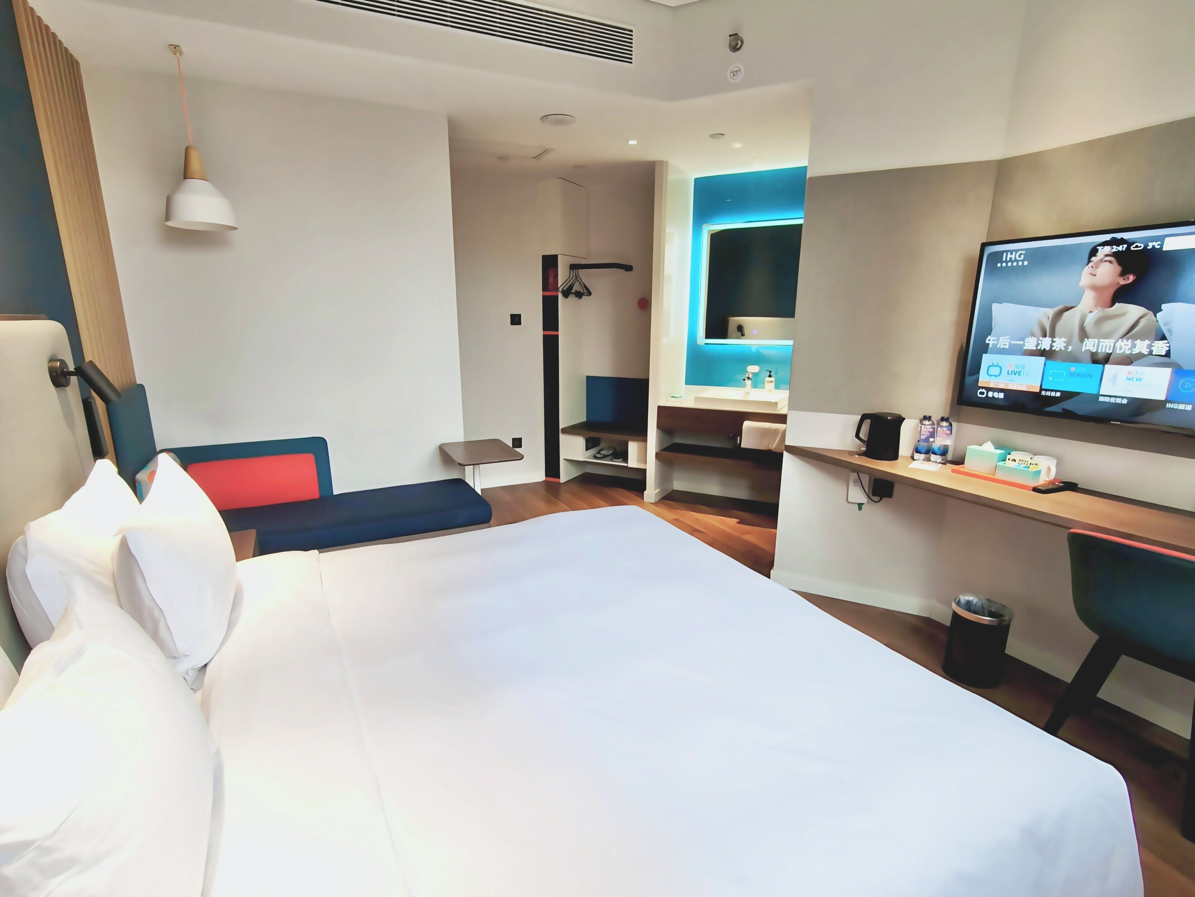 Een hotelkamer met een bed, een televisie, een bureau met stoel, een klein tafeltje en een spiegel.