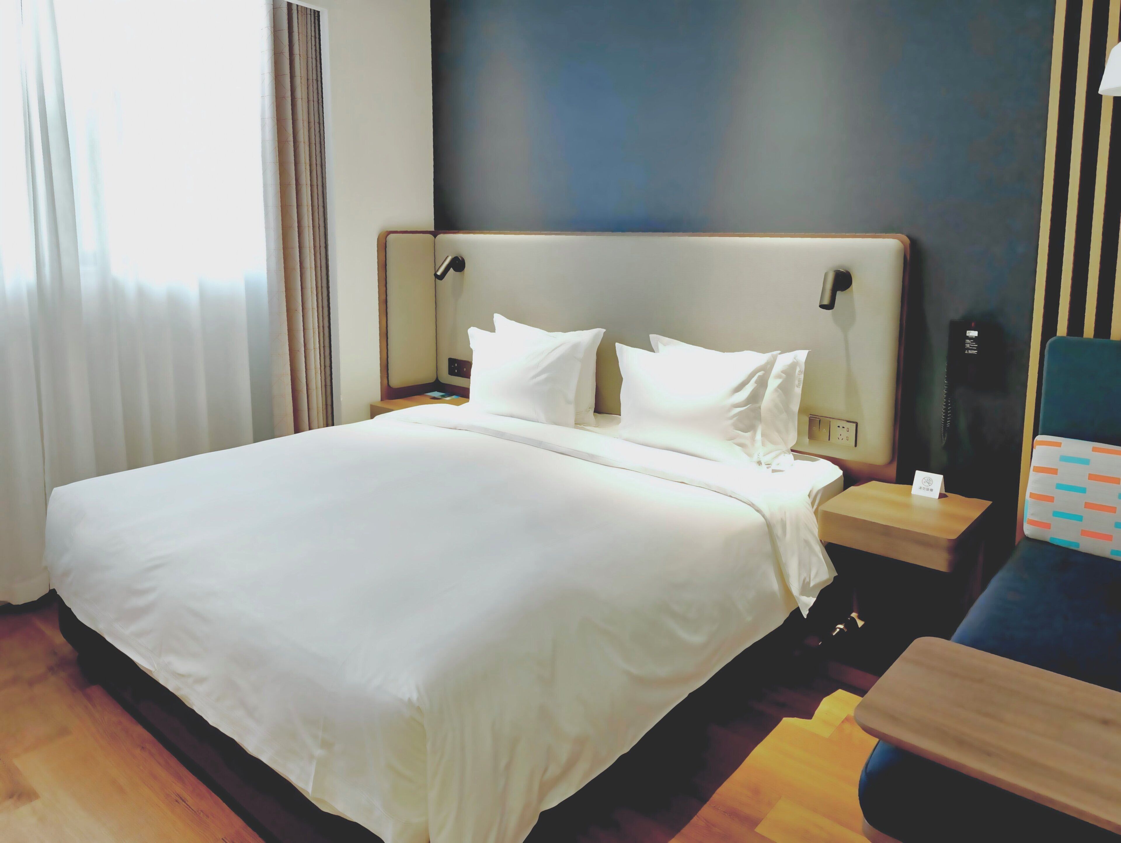 A hotel room with a large bed, a bedside table, a nightstand, and a small desk with a chair.