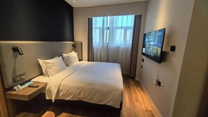Une chambre d’hôtel moderne avec un grand lit, une table de chevet avec une lampe, un téléviseur fixé au mur et une fenêtre avec des rideaux.
